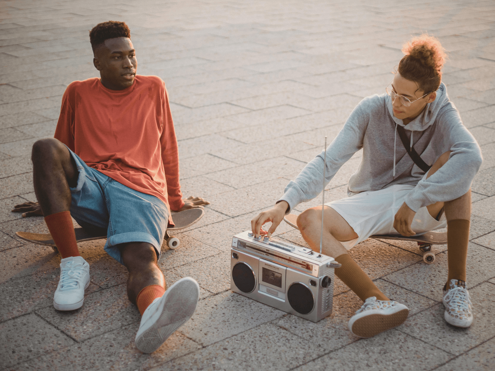 zwei Jugendliche sitzen mit Skateboards auf dem Boden mit einem Radio in der Mitte