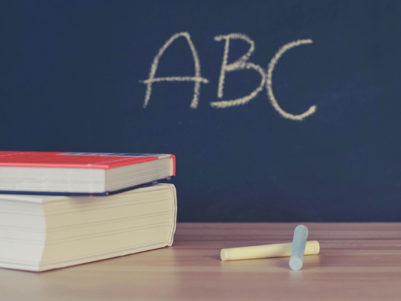 zwei Bücher und Kreide liegen auf einem Tisch vor der Tafel, auf der ABC steht