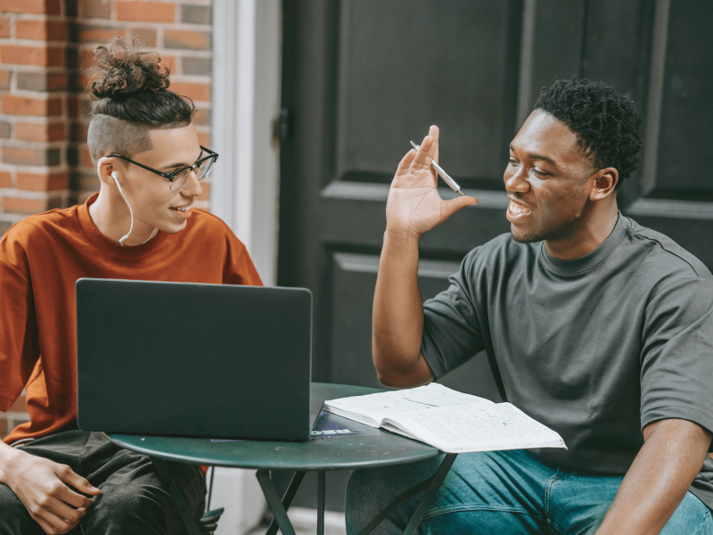 Zwei Schüler sitzen vor dem Laptop und unterhalten sich über digitale Bildung