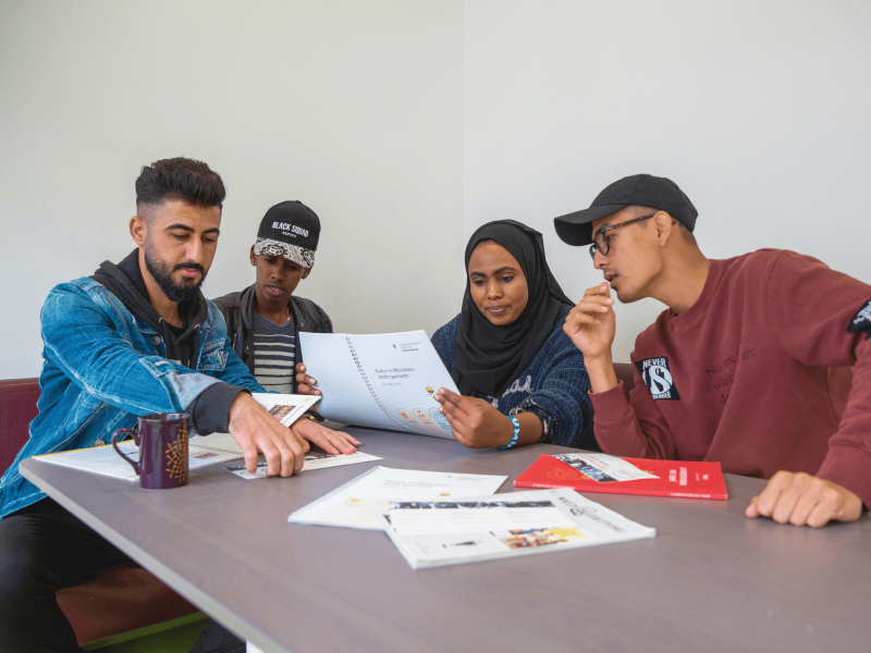 DaZ-Lernende sitzen zusammen an einem Tisch im Klassenraum und arbeiten an einer Mathematik in DaZ Aufgabe