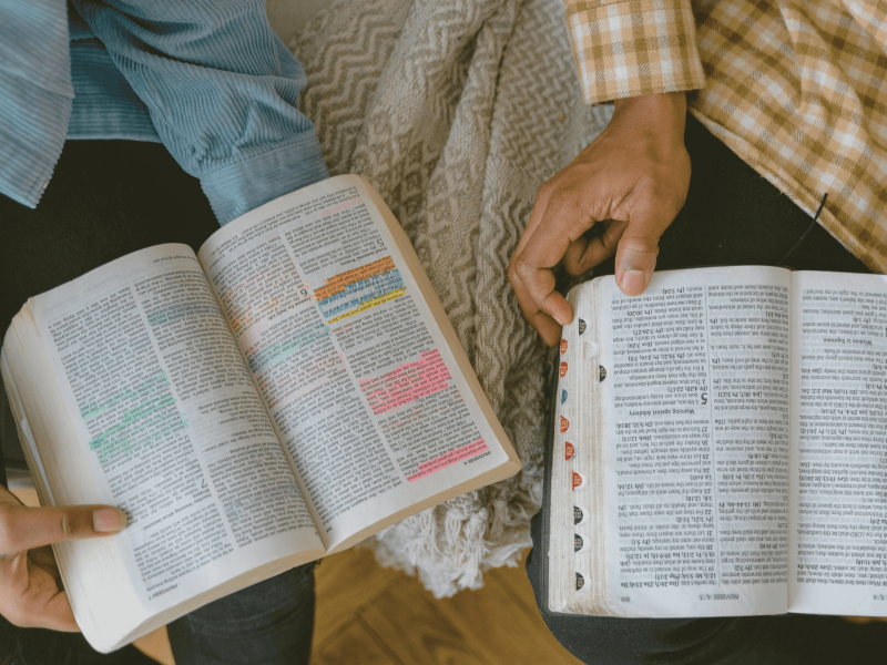 Zwei Bücher mit bunt markierten Stellen liegen aufgeschlagen auf dem Schoß von zwei Personen