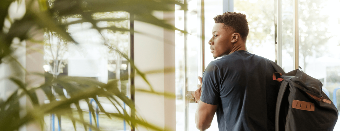 ein junger schwarzer Mann mit Rucksack verlässt ein Gebäude