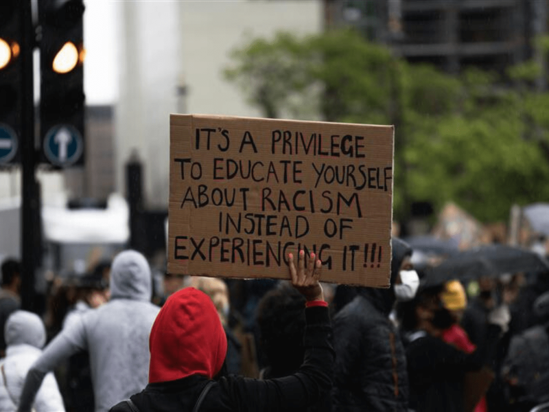 Ein Schild wird hochgehoben auf dem "It's a privilege to educate yourself about racism instead of experiencing it" steht