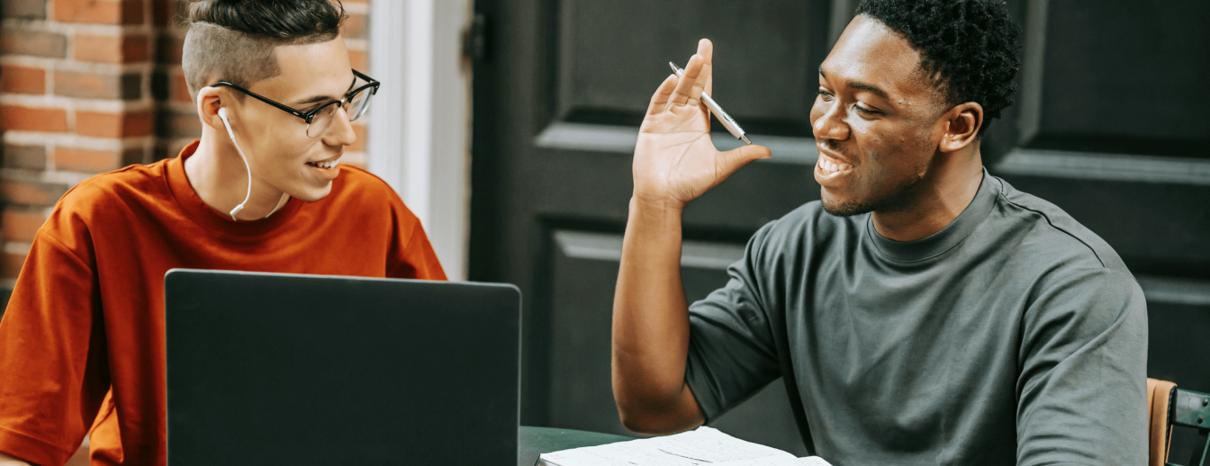 Zwei Schüler sitzen vor dem Laptop und unterhalten sich über digitale Bildung