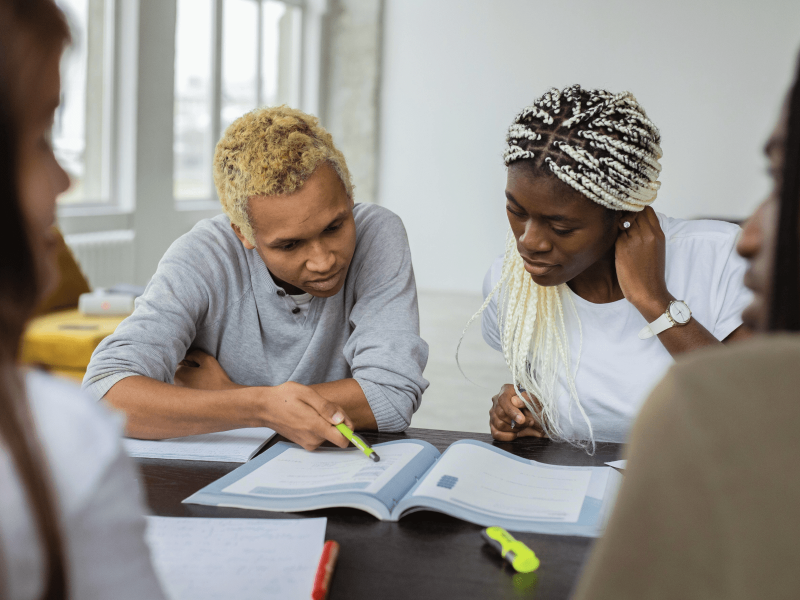zwei DaZ-Lernende sitzen an einem Tisch und schauen gemeinsam in ein DaZ Lehrwerk